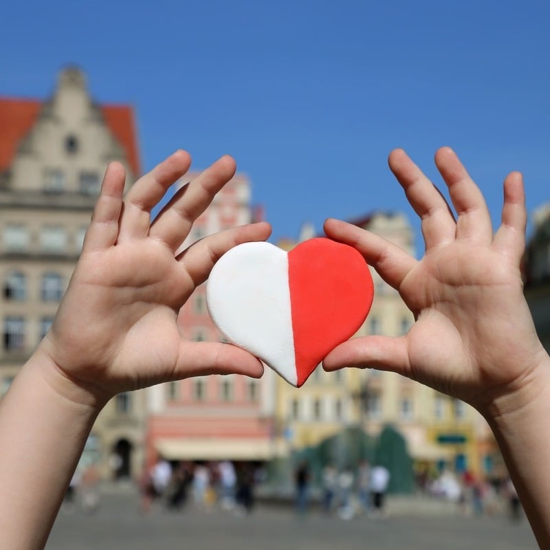 A Person Holding A Red And White Heart, The Colors Of The Polish Flag, In The Central Square In Warsaw, Poland, Eastern Europe