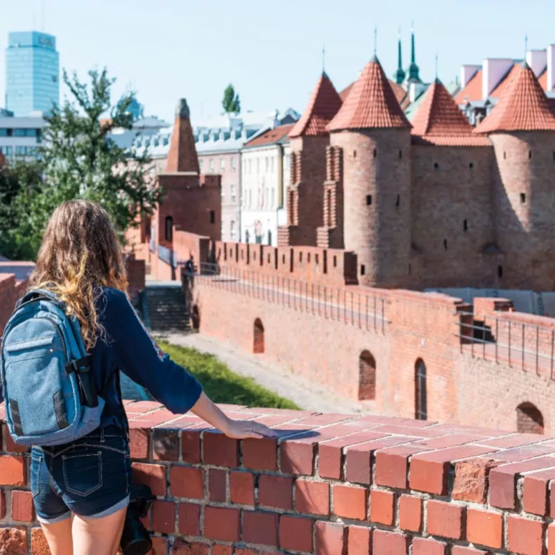 Warsaw, Poland Famous Barbican old town historic capital city during sunny summer day and red orange brick wall fortress architecture with young woman travel tourist backpack