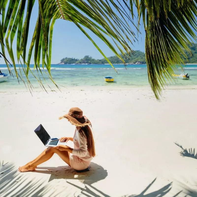 woman on laptop on beach with boats