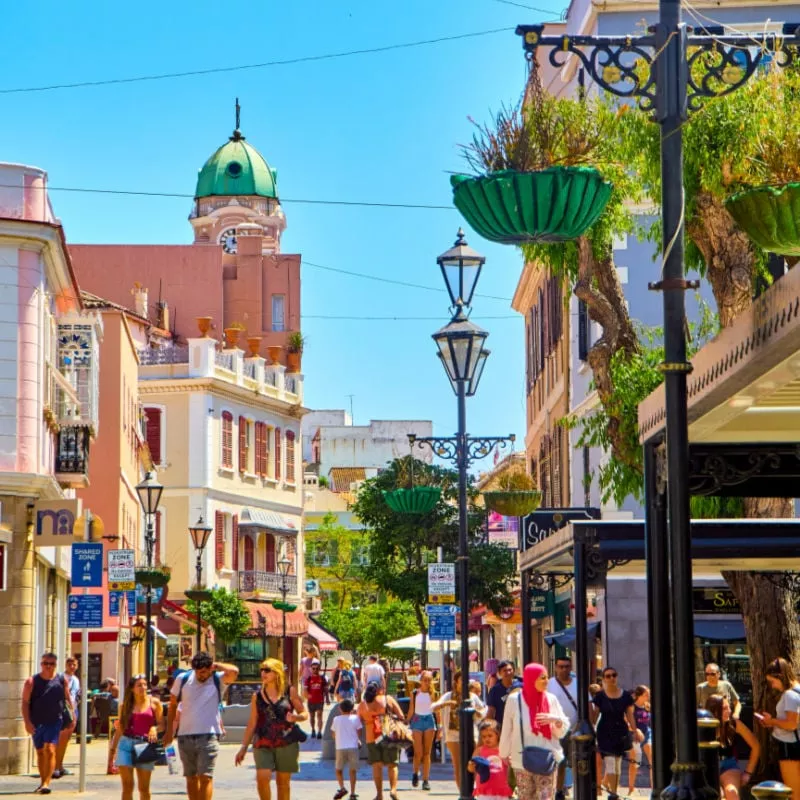 Tourists walking on Main Street at sunny day, with the Belfry of Saint Mary the Crowned Cathedral in the background. Gibraltar downtown