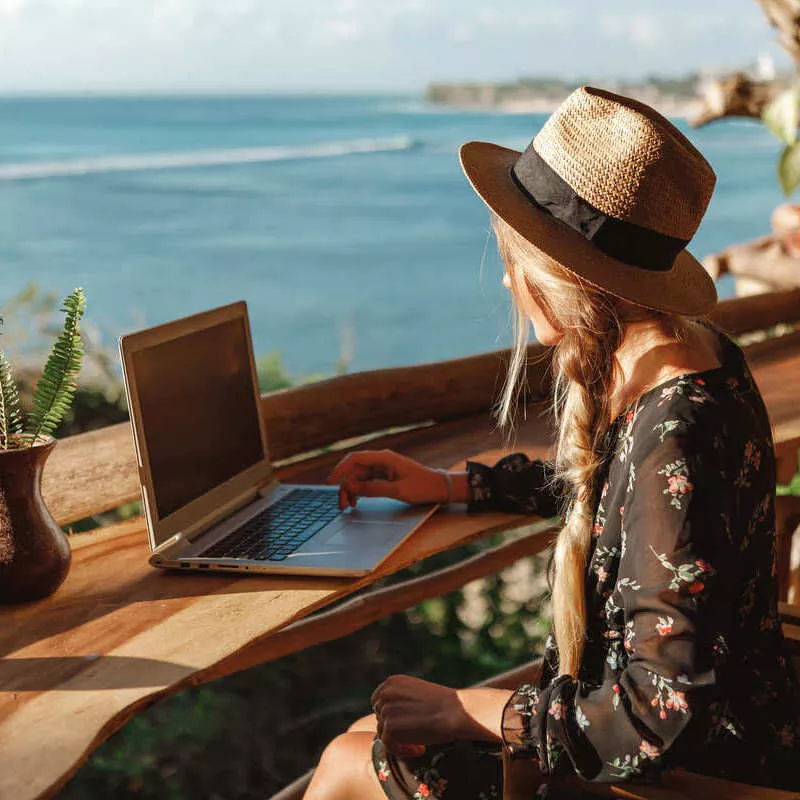 Young Woman Working From Her Computer By The Beach In Unspecified Location