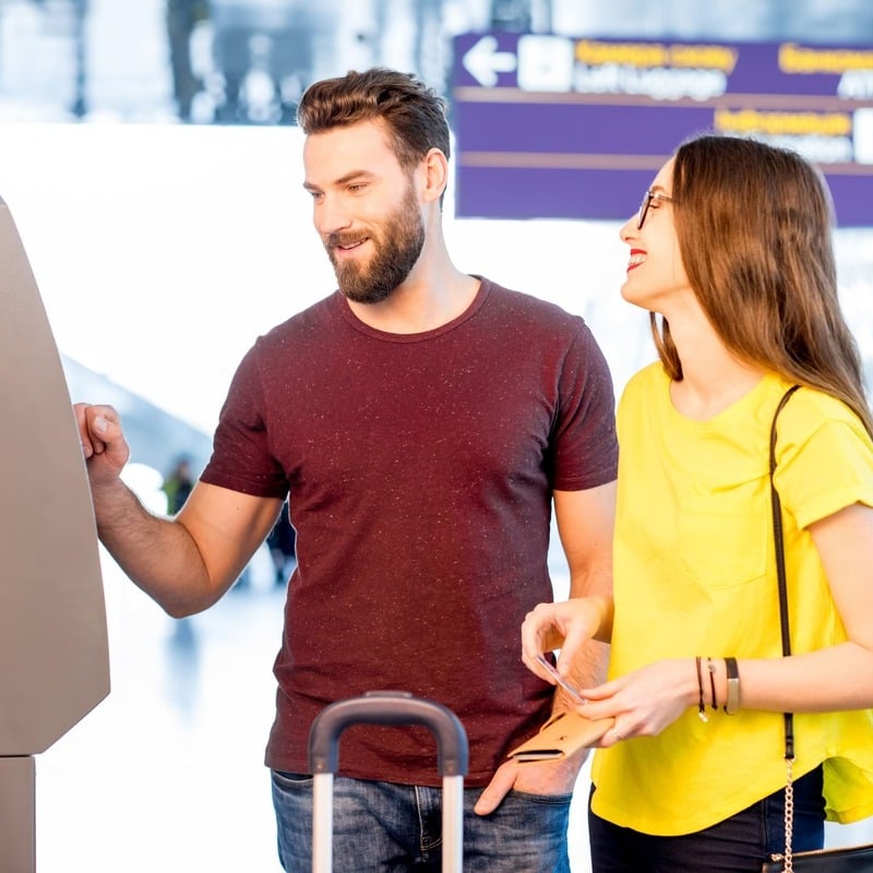 Couple Of Travelers Pictured Beside Their Luggage As They Withdraw Money From An ATM At The Airport, International Travel