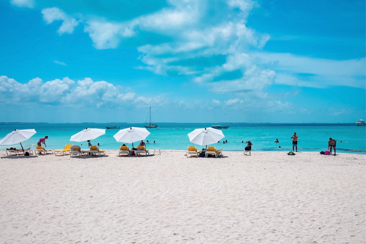 Cancun, Mexico. Deckchairs under canopy shade for resting on beach sand in front of sea with yachts. Tourists enjoying beach holiday