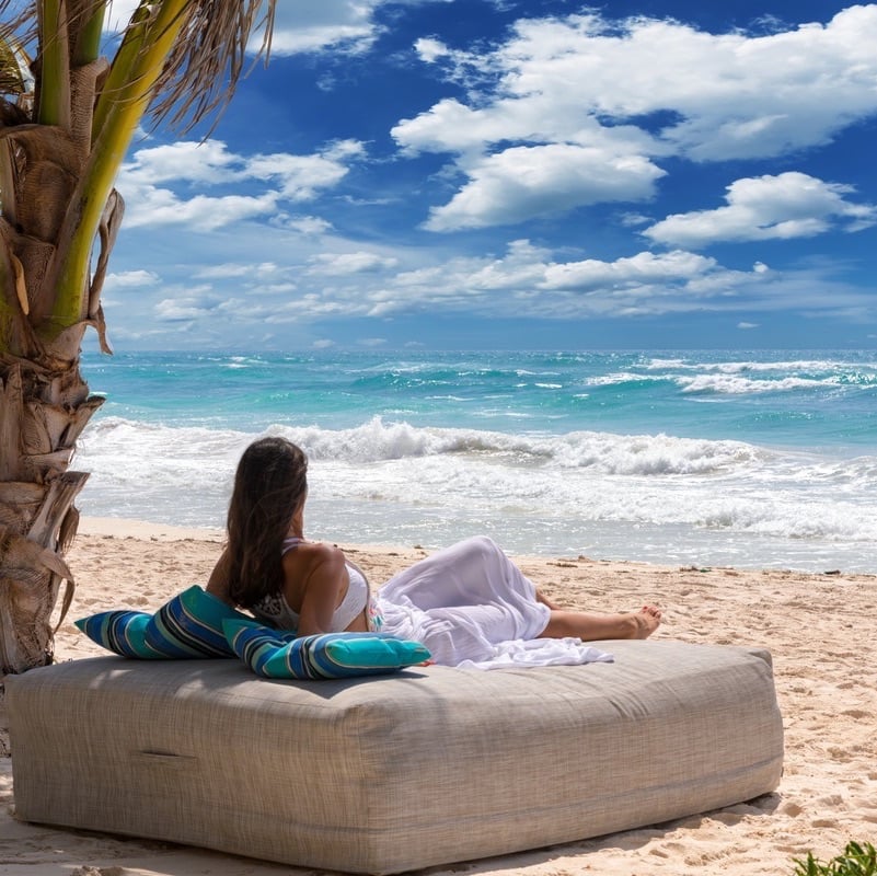 Woman is relaxing on a luxurious sunbed under a palm tree on a tropical beach