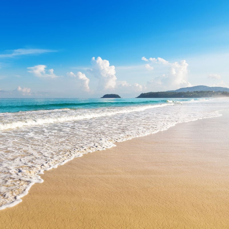 foamy white water washes ashore onto a sandy beach with the turquoise sea in the backgroung