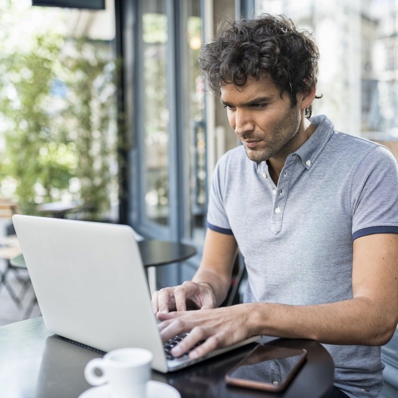 A Young Handsome Man Working With His Laptop From A Cafe In France, Digital Nomad In Europe