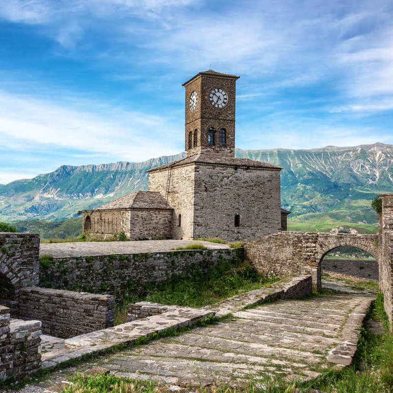 Clock Tower In The Inner Citadel Of Gjirokaster Castle Set Against The Backdrop Of Green Mountains, In The Old Town Of Gjirokaster, Albania, South Eastern Europe