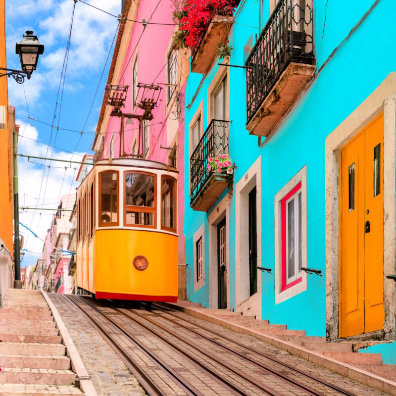 Lisbon, Portugal - Yellow tram on a street with colorful houses and flowers on the balconies - Bica Elevator going down the hill of Chiado