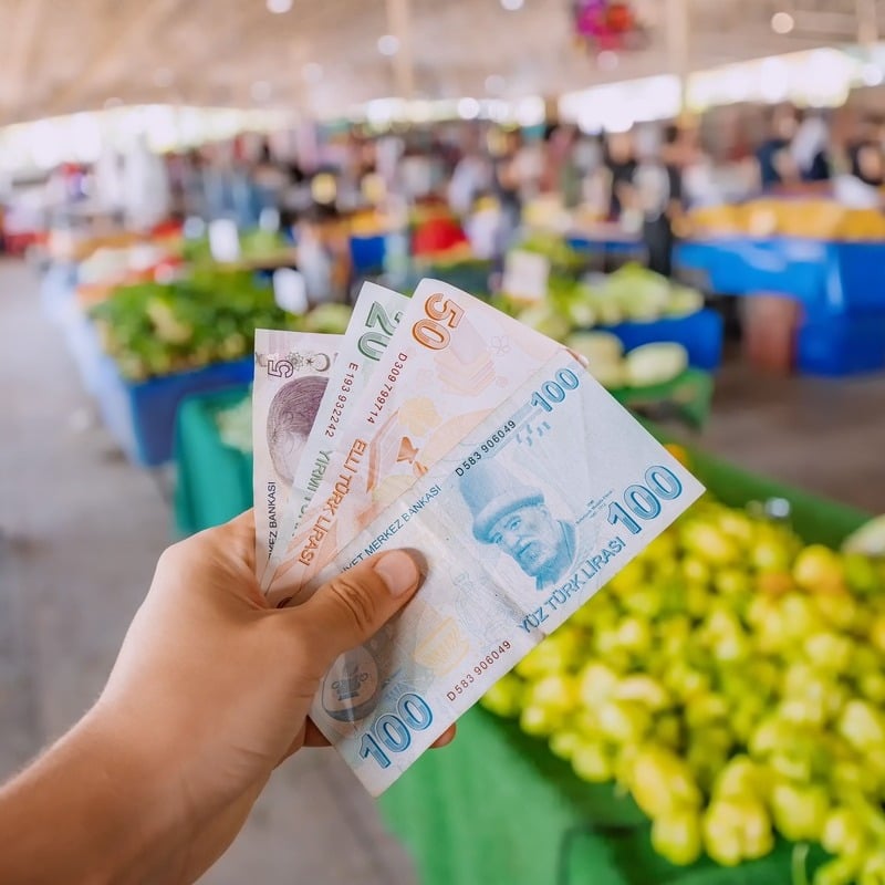 An Individual Holding Up Turkish Liras In A Fruit Market In Turkiye, Turkey Or North Cyprus