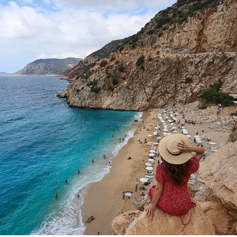 Girl in red dress and hat posing and watching panorama landscape of Kaputas Beach, Turkiye.