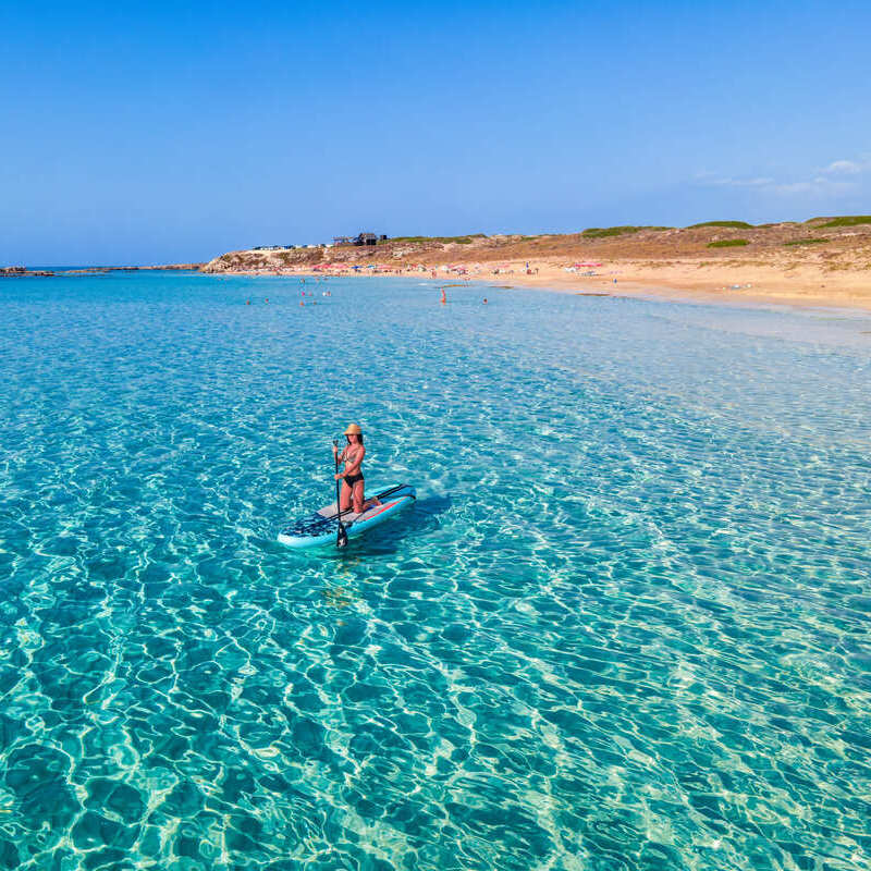 Young Woman Paddleboarding In The Turquoise Waters Of The Mediterranean Sea Off The Coast Of North Cyprus, Southern Europe