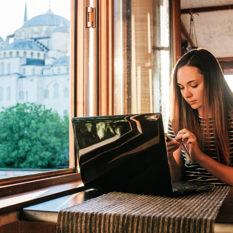 Young woman-blogger-freelancer working on a laptop in a cafe in Istanbul and calling by phone. View from the window to the world-famous Blue Mosque