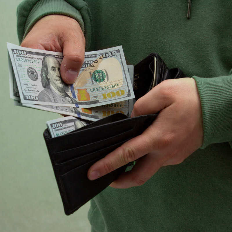 A man holding a wallet and 100-dollar bills