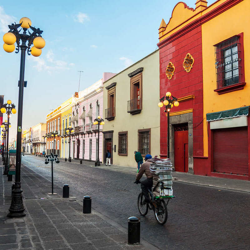 A Mexican Local Riding A Bike Down A Colonial Era Street In Puebla, Mexico, Latin America