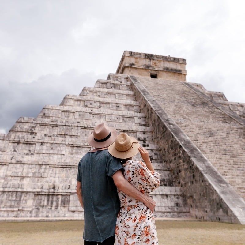 A Young Couple Embracing As They Gaze At The Mayan Pyramid In Chichen Itza, Yucatan Peninsula, Mexico