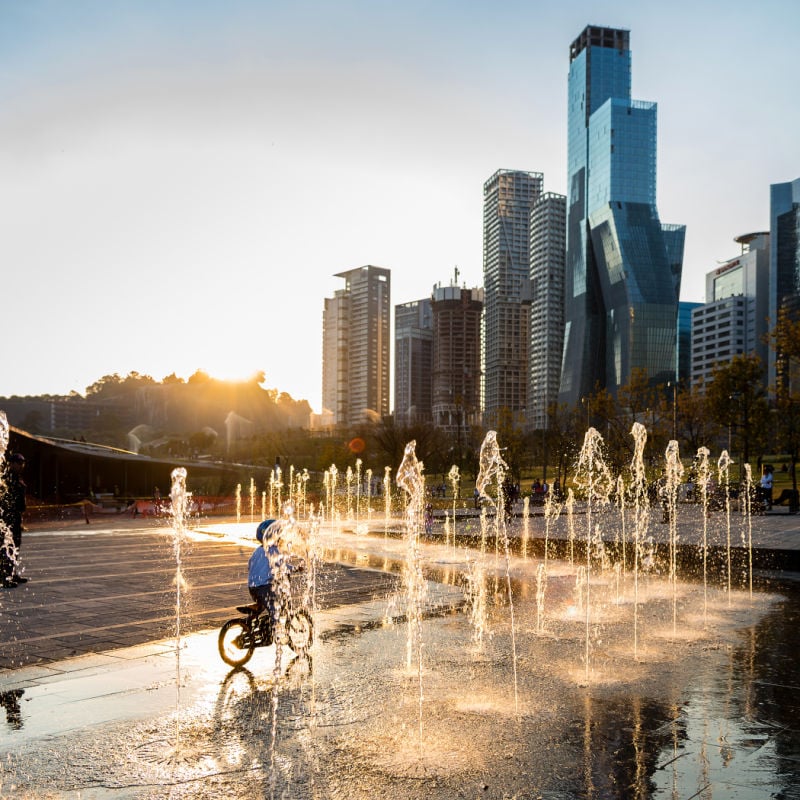 child riding on bicycle through fountains with skyscrapers in the background in mexico city