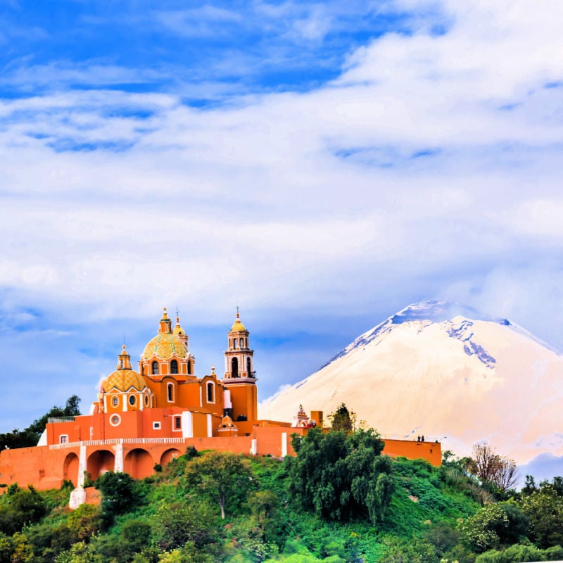 cholula cathedral Puebla with the popocatepetl volcano, exuding smoke in the background