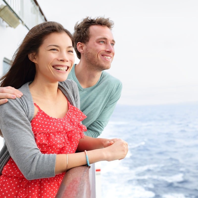 A Young White Man And Young Asian Woman, Couple Traveling On A Ferry Or Cruise Ship As They Smile In An Unspecified Location