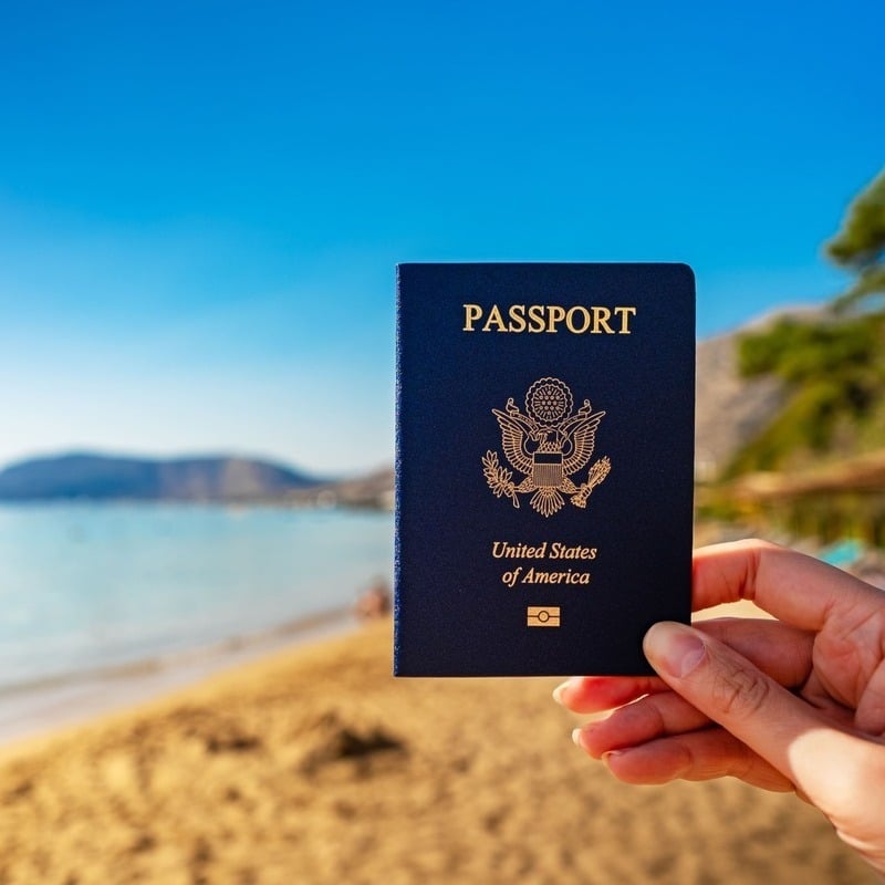 An American Traveler Holding Up A U.S. American Passport In A Beach Location, Unspecified Location.jpg