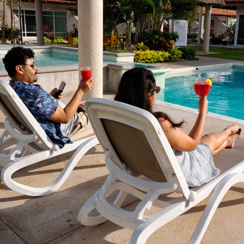 Vacationing Couple Drinking Cocktails By The Poolside In A Resort