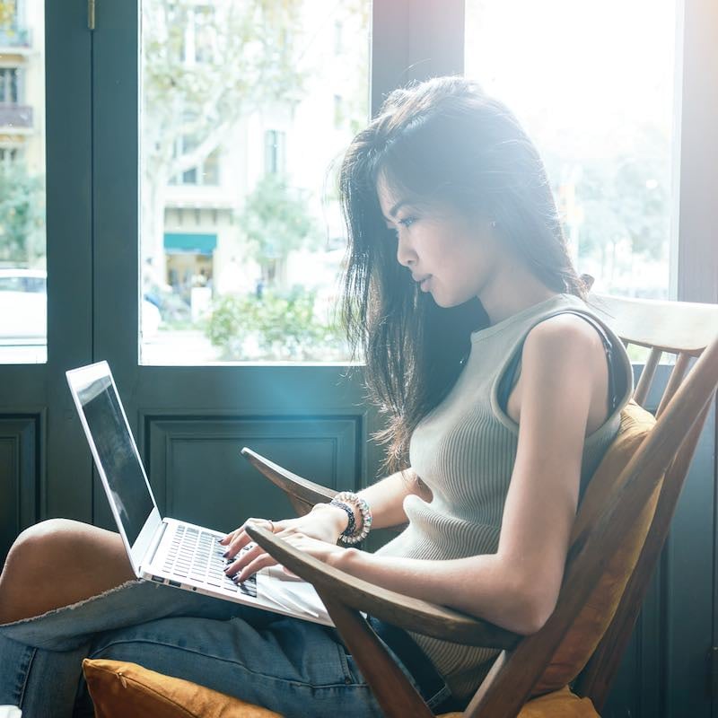 Young Asian Woman Working From. Her Computer From A Cafe In An Unspecified Location