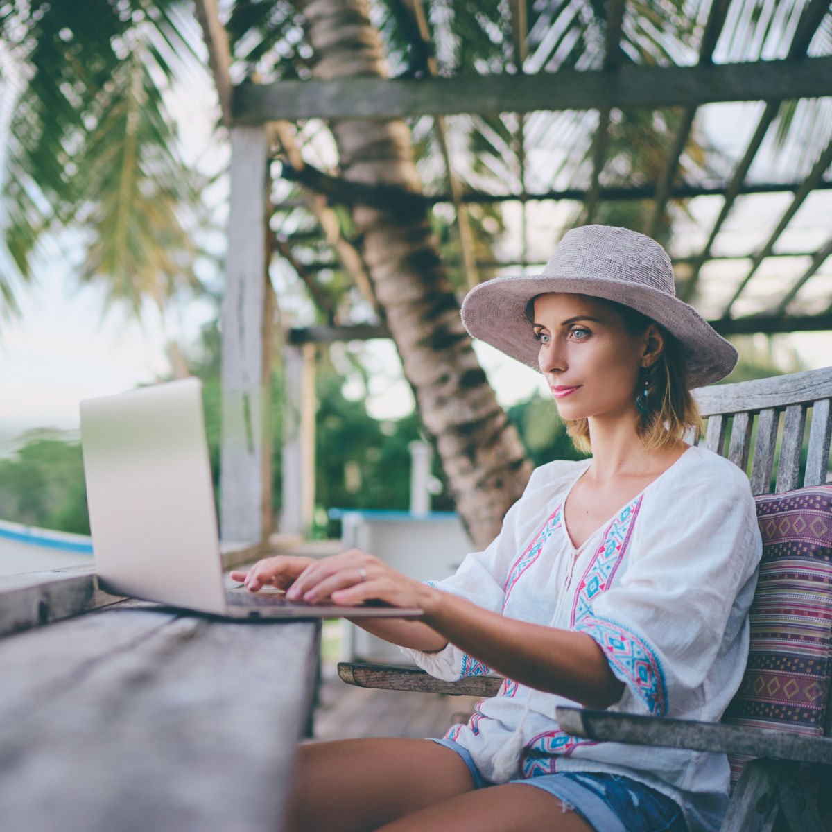 Female digital nomad with laptop sitting under palm tree