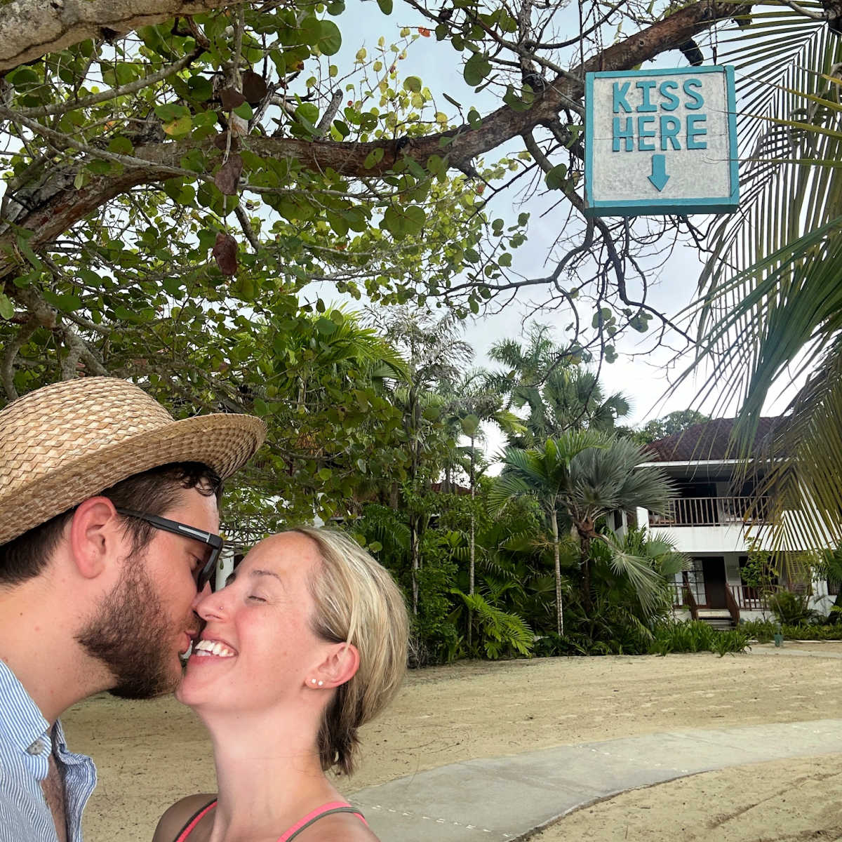 Tyler and Liz fox under a 'Kiss Here' sign in Negril, Jamaica