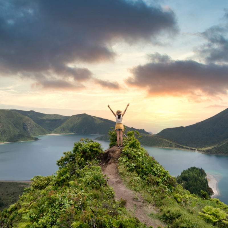 woman traveler holding hat and looking at amazing mountains and forest, wanderlust travel concept, space for text, atmospheric epic moment, azores ,portuhal, ponta delgada, sao miguel