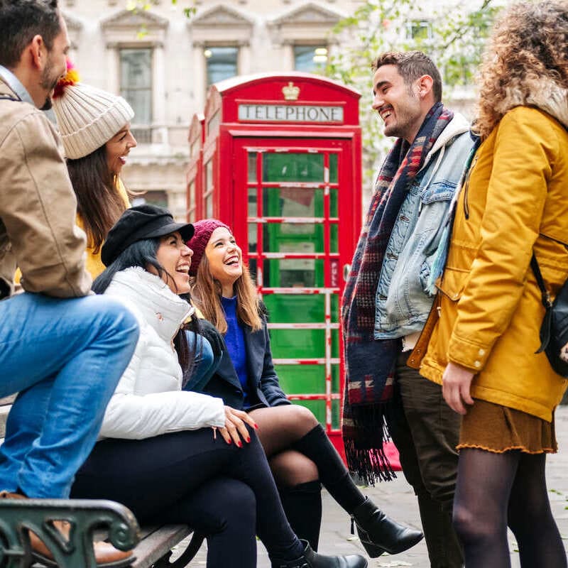 A Group Of Friends Smiling And Chatting Near A Red Telephone Box In London, England, United Kingdom