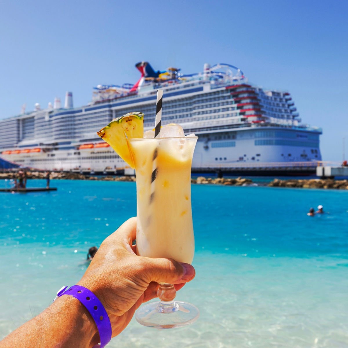 Close-up view of hand holding glass of alcoholic cocktail on Caribbean beach with cruise ship