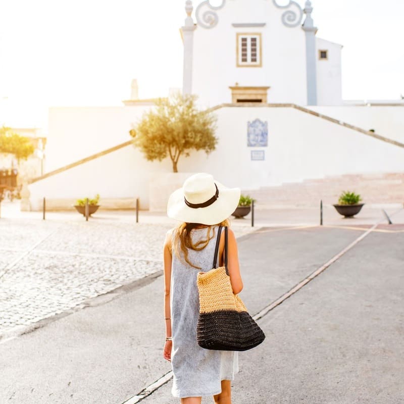 Young Woman Walking Towards A Whitewashed Church In Albufeira, Portugal