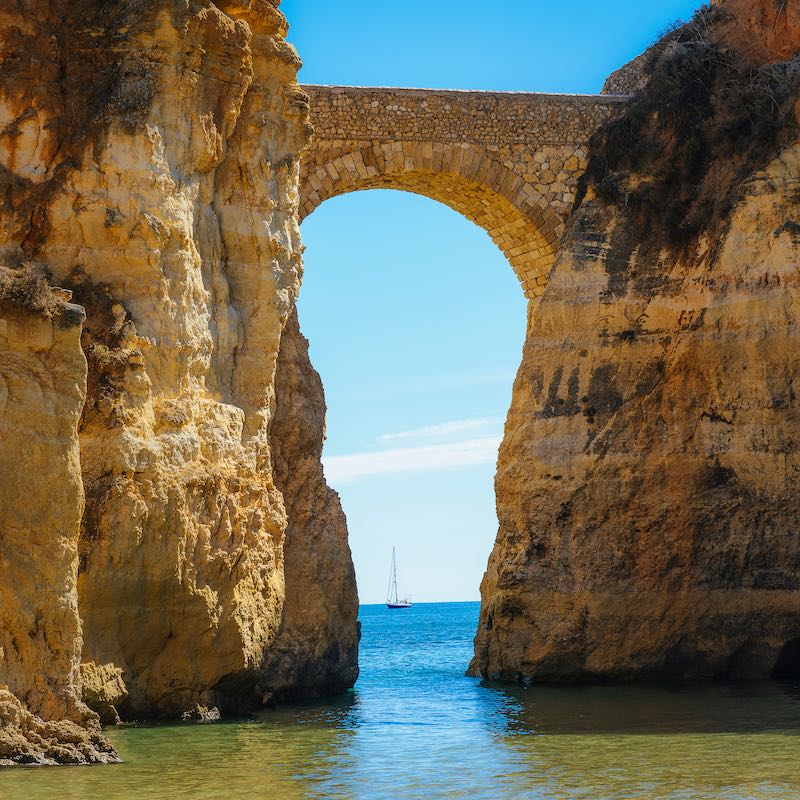 Detailed View of arched bridge with sailboat in Students Beach in Lagos, Algarve, Portugal